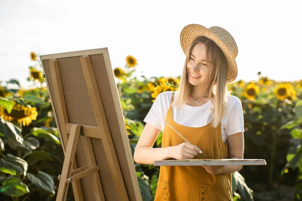 Bir kadın ayçiçeği tarlasında duruyor ve resim çiziyor. Tuval bir sehpanın üzerinde duruyor. O gülümsüyor ve resme bakıyor. Elinde fırça tutuyor..