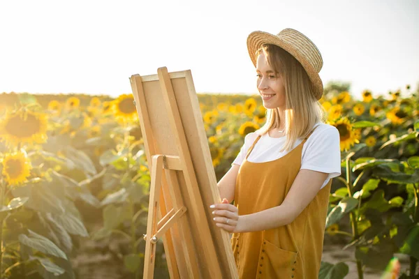 Genç bir kadın tabloyu sehpaya koyuyor. O, bir ayçiçeği tarlasının ortasında duruyor. Gülümsüyor..