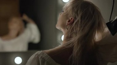 Güzel bir kız stüdyoda soyunma odasında oturuyor ve saçını bir saç kurutma makinesiyle kurutuyor. O, aynaya bakıyor. Kamera onun saçına odaklanıyor. 4K