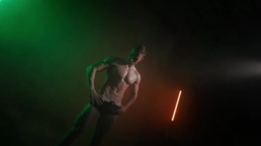 Çıplak vücutlu bir sporcu aşağıdadır ve aşağıya bakar. O, ellerini kemerinde tutuyor. Kamera dönüyor ve ona yaklaşıyor. Turuncu ve yeşil ışık onun üzerinde parlıyor. 4K