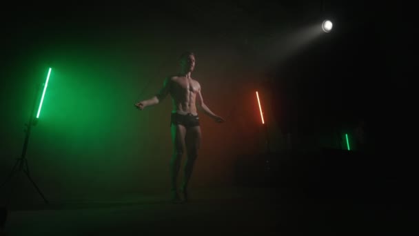 한 운동 선수가 로프 위에서 뛰고 있습니다. 심장외과 훈련. 근육 이 어떻게 움직이는지 보 세요. 오렌지와 녹색 빛 이 그 의 위에 빛나고 있습니다. 4K — 비디오