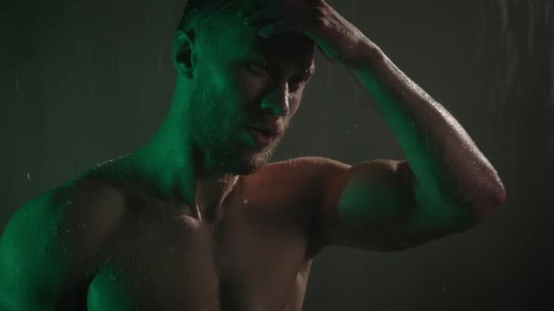 スポーティな男が手で髪を調整している。カメラが動いている。水が彼の体を流れている。緑の光が彼の上に輝いている。4K — ストック動画
