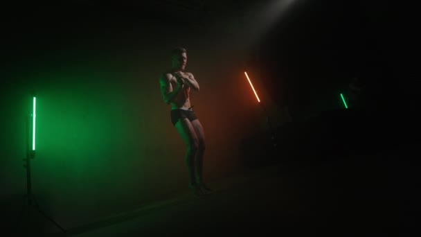 Een atleet springt op het touw. Hij zwaait ermee. Cardio training. Een oranje en groen licht schijnt op hem. 4K — Stockvideo