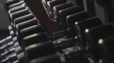 Sportif bir adam raftan ağır dambıllar alıyor. Zor bir yaklaşım için hazırlanıyor. Spor salonunda antrenman. Yakın plan çekim. 4K