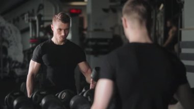 Sportif bir adam kol egzersizi yapıyor ve halterleri değiştiriyor. O, aynanın önünde duruyor ve egzersizin doğru uygulanmasını izliyor. 4K