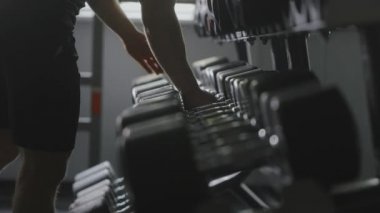 Sportif bir adam halterlerden ağır dambıllar alıyor ve zor bir yaklaşım sergiliyor. Spor salonunda antrenman. 4K