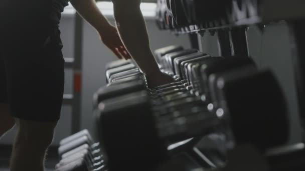 A sporty man is taking heavy dumbbells from the rack and go to do a difficult approach. Training in the gym. 4K — 图库视频影像