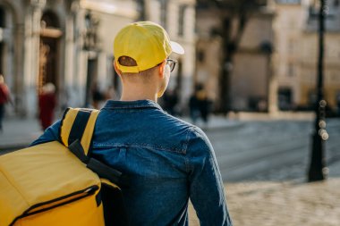 Genç teslimatçı gidiyor. Güneş ışıl ışıl parlıyor. O, omuzlarında teslimat için sarı bir sırt çantası taşıyor. Arkadan ateş ediyorlar..