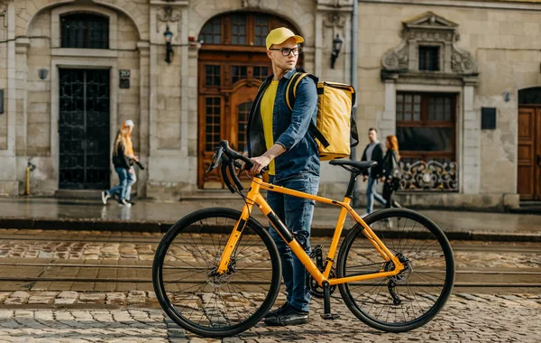 Bir kurye eski kasabanın merkezine doğru yürüyor ve yanında bir bisikletle. O, omuzlarında teslimat için sarı bir sırt çantası taşıyor. Arkadan ateş ediyorlar..