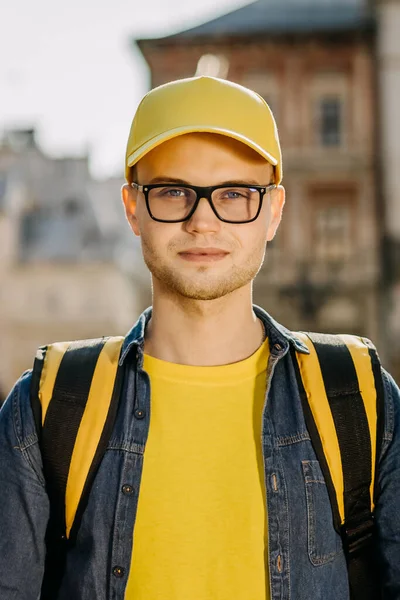 Ayakta duran ve gülümseyen bir teslimatçının portresi. O, sarı elbise giyiyor. Eski şehrin merkezi. Dikey fotoğraf.
