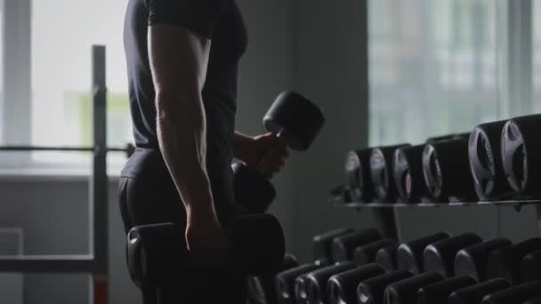 A man is standing in front of a mirror and concentrating on the biceps exercise with dumbbells. Training in the gym. The camera is moving from bottom to top. 4K — 图库视频影像
