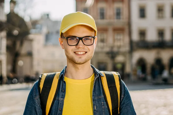 Ayakta duran ve gülümseyen bir teslimatçının portresi. O, sarı elbise giyiyor. Merhaba gülümsüyor. Eski şehrin merkezi..