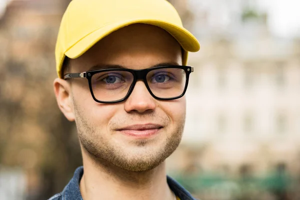 Ayakta duran ve gülümseyen bir teslimatçının portresi. Sarı bir şapka ve gözlük takıyor. Yakın çekim..