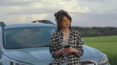 Arabanın yanında duran ve kırsal kesimde akıllı telefon kullanan bir kadın.