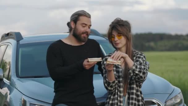 Пара веселится во время еды бутерброды возле современного автомобиля — стоковое видео