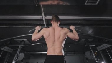 Sporcu yatay çubukta barfiks çekiyor. Kaslarının nasıl çalıştığını görebilirsiniz. Spor salonunda antrenman. Arkadan ateş ediyorlar. 4K