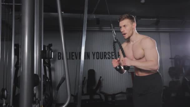 The sportsman is doing an exercise for the triceps. He is extending his arms out in a crossover. Training in the gym. 4K — Video Stock