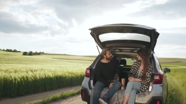 Man and woman sitting in car trunk smiling and talking — Stockvideo