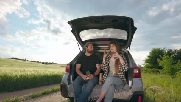 Couple sitting in car trunk and relaxing among green field — Stockvideo