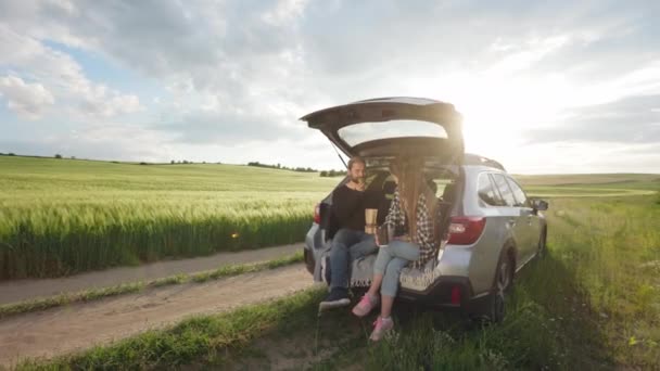 Couple drinking coffee and eating snack in car among field — Stockvideo
