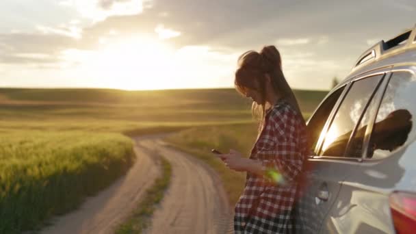 Frau benutzt Handy, während sie bei Sonnenuntergang neben Auto steht — Stockvideo