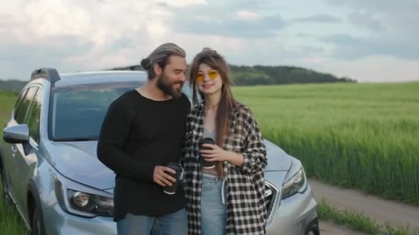 Lykkelig par som står i klemmer ved bilen og drikker kaffe – stockvideo
