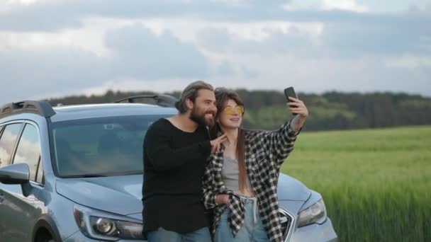 Positive couple taking selfie near car among green field — Stock Video