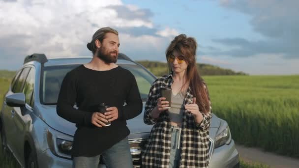 To kjærlige mennesker som står nær bilen blant grønne jorder – stockvideo
