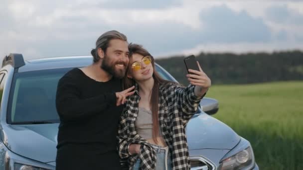 Alegre pareja tomando selfie cerca de coche entre el campo — Vídeos de Stock