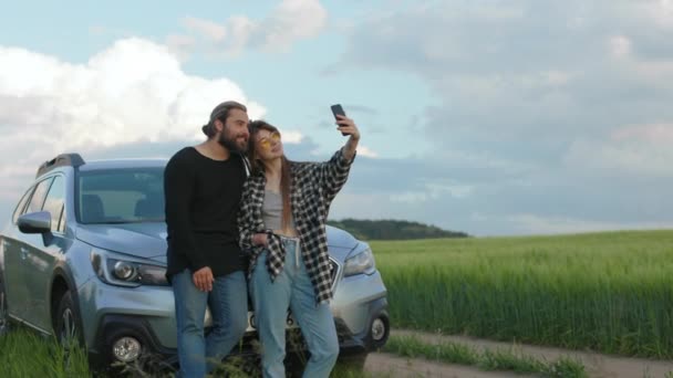Mutlu insanlar kırsal kesimde arabanın yanında selfie çekmek için cep telefonu kullanıyorlar. — Stok video