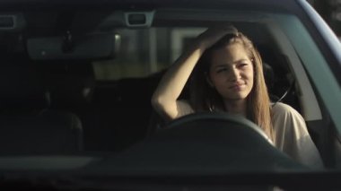 Genç bir kadın sürücü koltuğunda arabasında oturuyor. O yorgun ve eliyle saçını düzeltiyor. Güneş onun üzerinde parlıyor. 4K