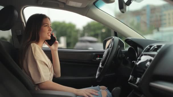Een jonge vrouw zit in de bestuurdersstoel. Ze praat emotioneel aan de telefoon en zwaait. 4K 50fps — Stockvideo