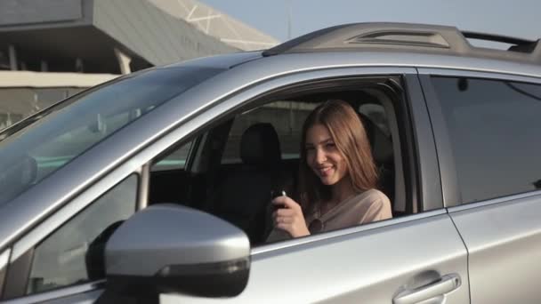 A young woman is sitting in the car in the drivers seat. She is showing her car key and smiling. She is looking at the camera. The camera zooms in. 4K — Vídeo de stock
