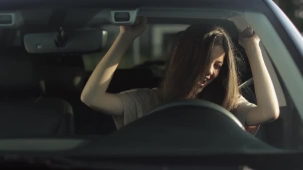 A happy woman is sitting in her car in the drivers seat and listening to music. She is waving her hands and head emotionally. 4K — Vídeo de stock