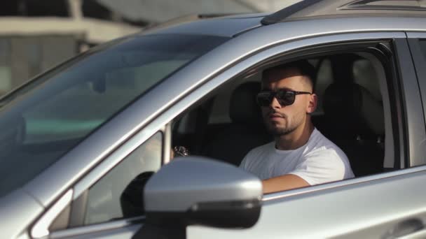 The man is sitting in the car in the drivers seat. He is turning his head and looking at the camera. Hes wearing sunglasses. 4K — Stockvideo