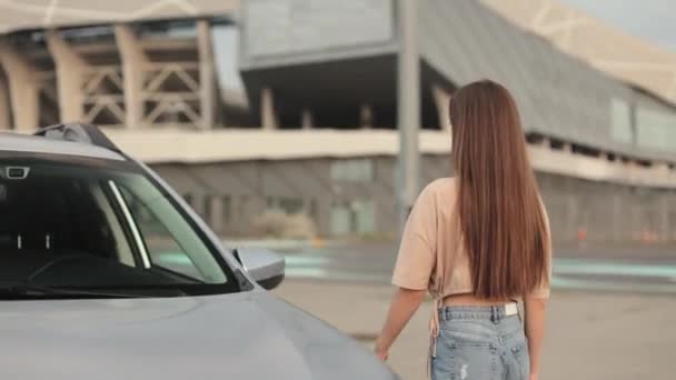 A young woman is going to the car. She is opening the door and sitting in the drivers seat. Car in the parking lot. The camera is moving to side her. 4K 50fps — Wideo stockowe