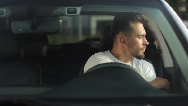Bir adam bir arabanın sürücü koltuğunda oturuyor. Emniyet kemerini takıyor ve ellerini direksiyona koyuyor. O, kameraya bakıyor. 4K 50fps — Stok video
