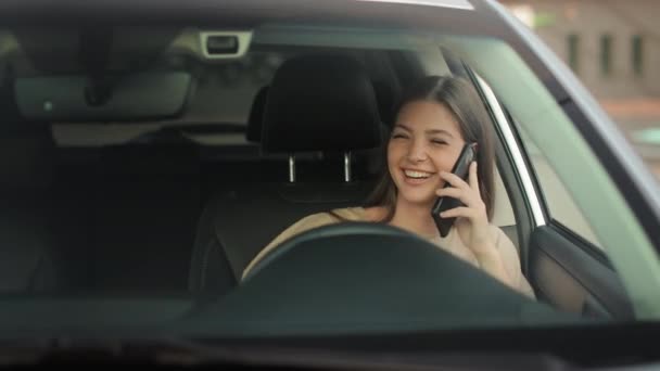 A young woman is sitting in the drivers seat. She is talking emotionally on the phone and waving. She is smiling. 4K 50fps — Vídeos de Stock