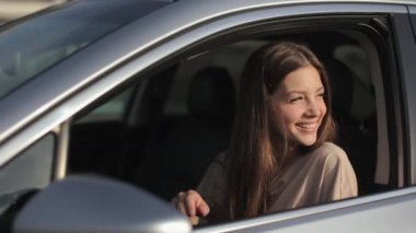 Genç bir kadın sürücü koltuğunda arabada oturuyor. Gülümseyen kadın başka tarafa bakıyor ve el sallıyor. Güneş onun üzerinde parlıyor. 4K