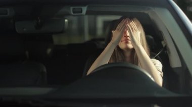 Genç bir kadın sürücü koltuğunda arabasında oturuyor. O, elleriyle kızgın bir şekilde direksiyona vuruyor ve yüzünü örtüyor. Hayal kırıklığına uğradı ve gözyaşlarını tutuyor. 4K