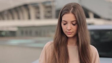 Otoparkta arabasının yanında duran genç bir kadının portresi. O, gülümseyerek kameraya bakıyor. Kamera onun etrafında hareket ediyor. 4K