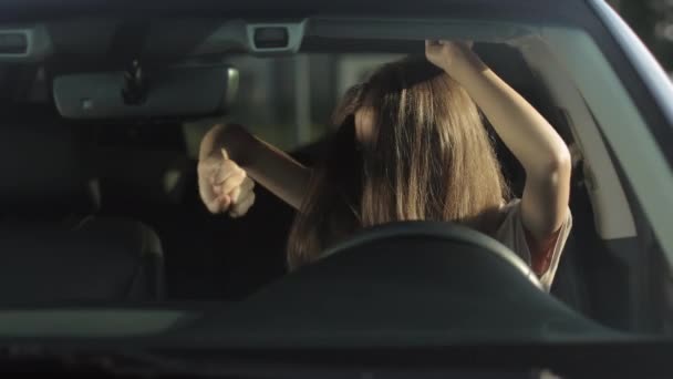 Μια χαρούμενη γυναίκα κάθεται στο αυτοκίνητό της στη θέση του οδηγού και ακούει μουσική. Χαμογελάει και χορεύει συναισθηματικά. 4K — Αρχείο Βίντεο