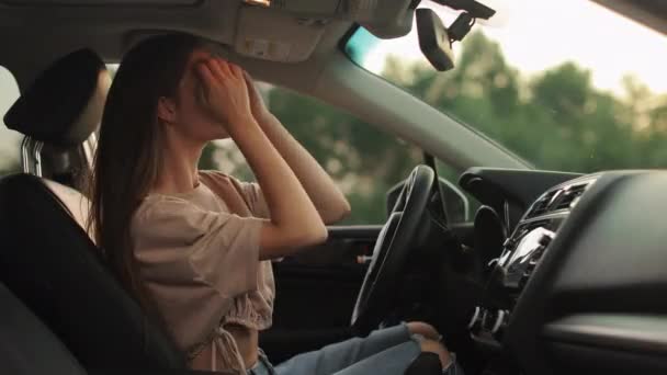 A young woman is sitting in the drivers seat. She is looking in the rearview mirror and adjusting her hair. Shooting from the side seats. 4K 50fps — Wideo stockowe