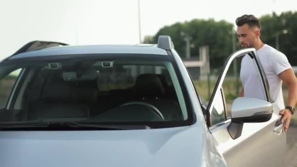 Un homme va à la voiture. Il ouvre la porte et s'assoit sur le siège du conducteur. Il pince sa ceinture. 4K 50fps — Video