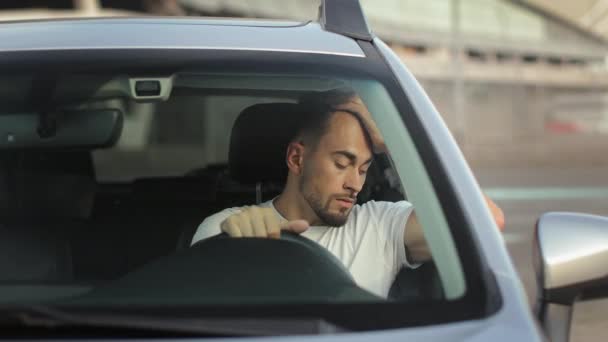 Ο άνθρωπος κάθεται στο αυτοκίνητο στη θέση του οδηγού. Είναι κουρασμένος και ακουμπά στην πόρτα με το χέρι του. Κρατάει το κεφάλι του. 4K 50fps — Αρχείο Βίντεο