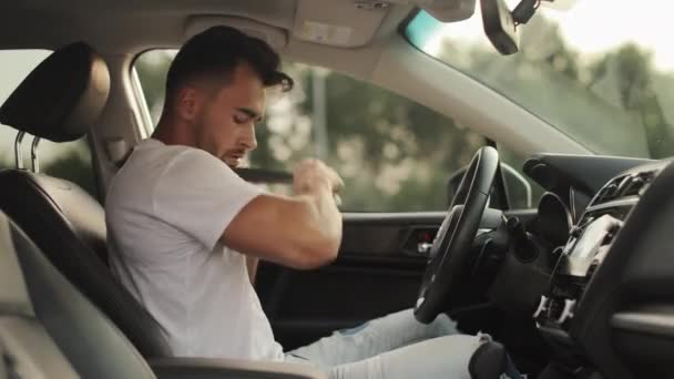 A man is sitting in the drivers seat of a car. He is putting on his seat belt and pressing the start button. Shooting from the side seats. 4K 50fps — Wideo stockowe