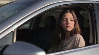 Genç bir kadın sürücü koltuğunda arabada oturuyor. Başını yana çeviriyor ve gülmeye başlıyor. Güneş onun üzerinde parlıyor. 4K