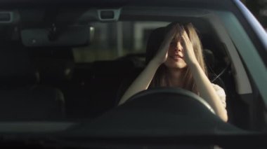 Genç bir kadın sürücü koltuğunda arabasında oturuyor. O, elleriyle kızgın bir şekilde direksiyona vuruyor ve yüzünü örtüyor. Hayal kırıklığına uğradı. 4K