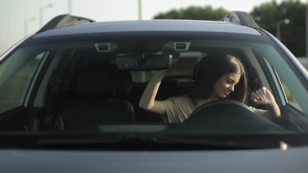 En lycklig kvinna sitter i sin bil i förarsätet. Hon lyssnar på musik och dans. Hon viftar med händerna och njuter av melodin. 4K — Stockvideo