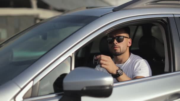 The man is sitting in the car in the drivers seat. He is looking at the camera and showing the car key. Focus on the key. 4K — Vídeo de stock